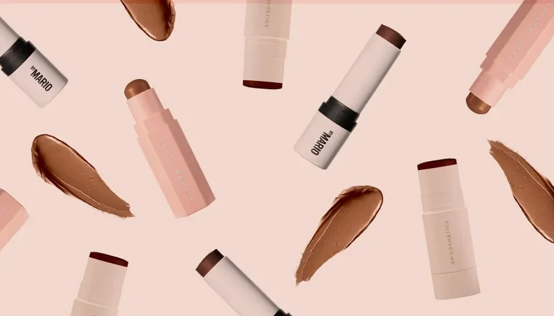 Best Contour Sticks 2024: Makeup contour sticks from Fenty Beauty, Makeup by Mario, and Em Cosmetics on a light pink background