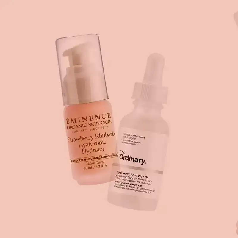 Best Hyaluronic Acid Serums 2024: Bottles of skin-care serums from The Ordinary and Eminence on a light pink background.