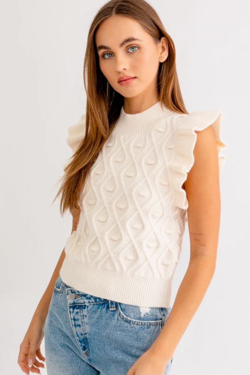 Mock Neck Ruffle Sleeve Cable Tank. The model is wearing a white sweater with a cable knit texture. She is also wearing blue jeans.