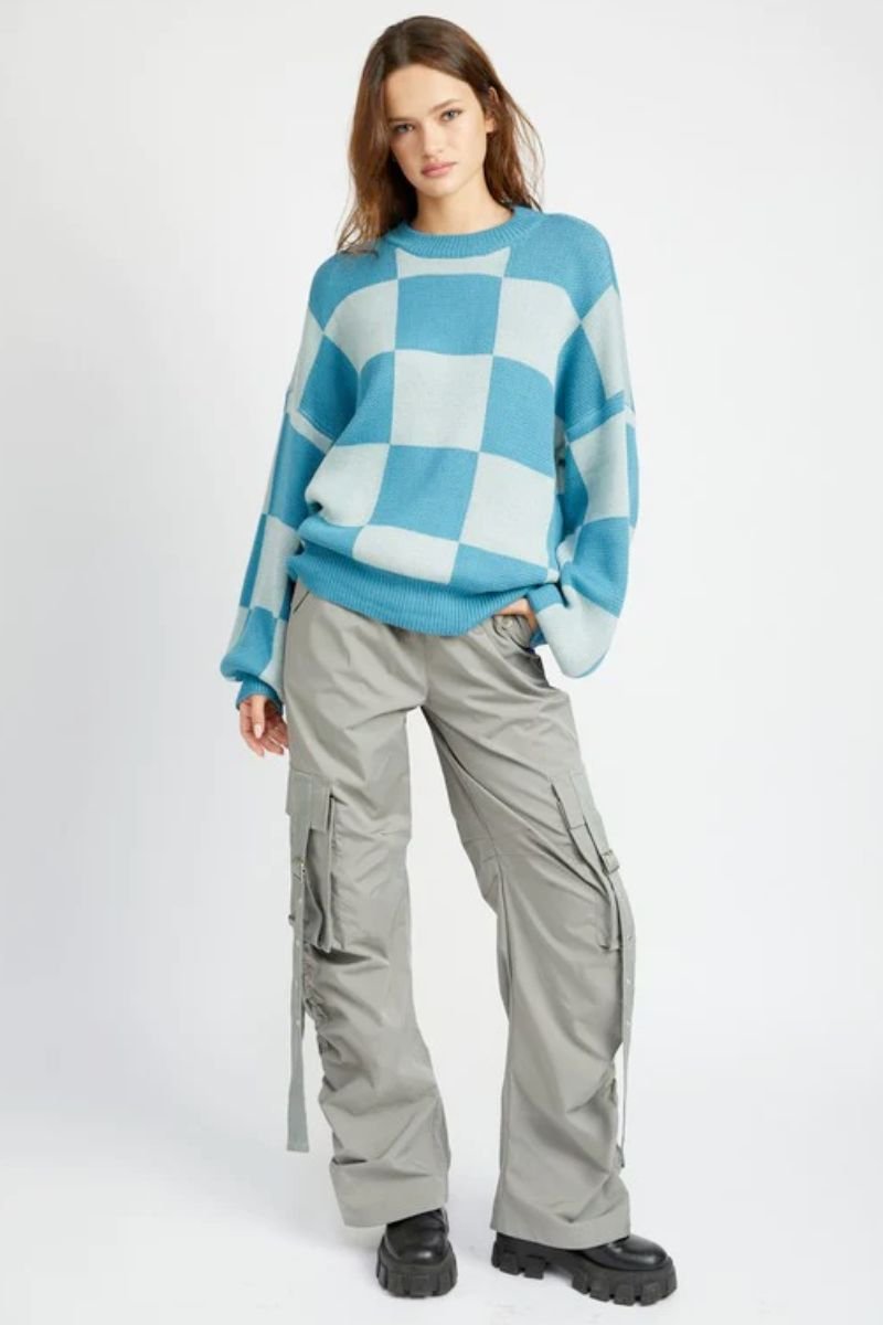 Checkered Sweater With Bubble Sleeves. There is a model in a blue and white sweater and grey cargo pants. She is also wearing chunky black boots.