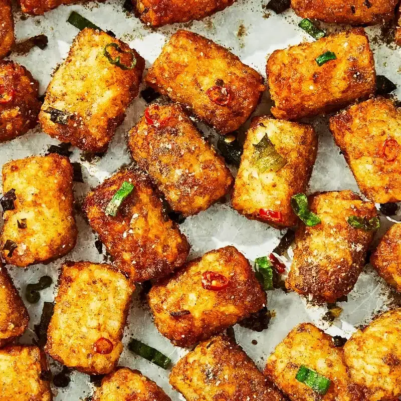 A close up of tater tots on a sheet tray with seasoning on them