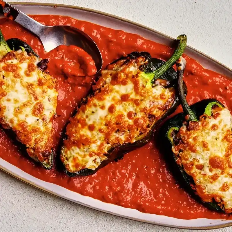 Black Bean and Cheese Rellenos Stuffed Chiles on a plate full of tomato sauce