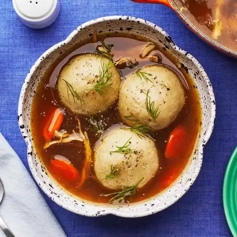 Matzo ball soup in a speckled bowl on a blue fabric