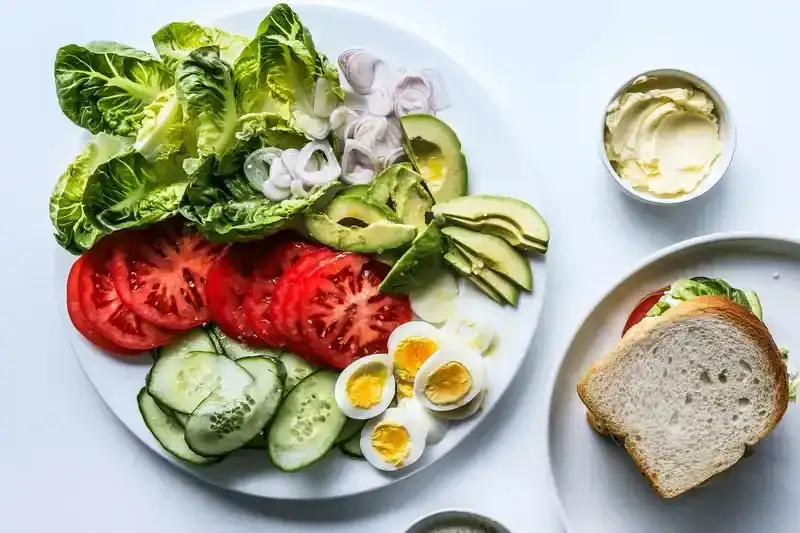 A platter with an easy lunch spread for making your own sandwiches with lettuce, sliced tomato, avocado, boiled eggs, shallots, and more.