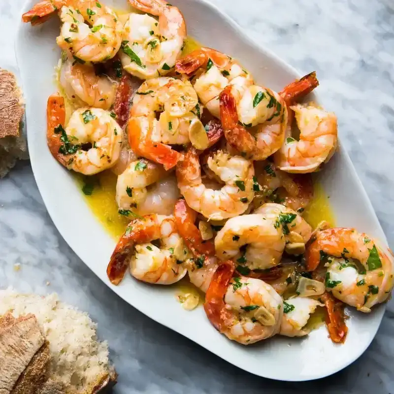 A pile of shrimp scampi on a platter with torn bread on the side for sopping.