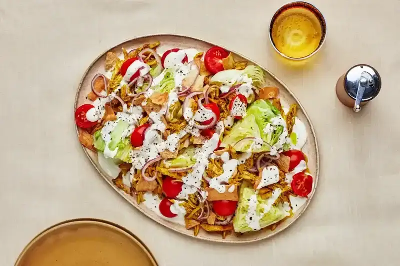 A Halal Cart Chicken Salad on a beige plate with water glass and pepper mill off to the side