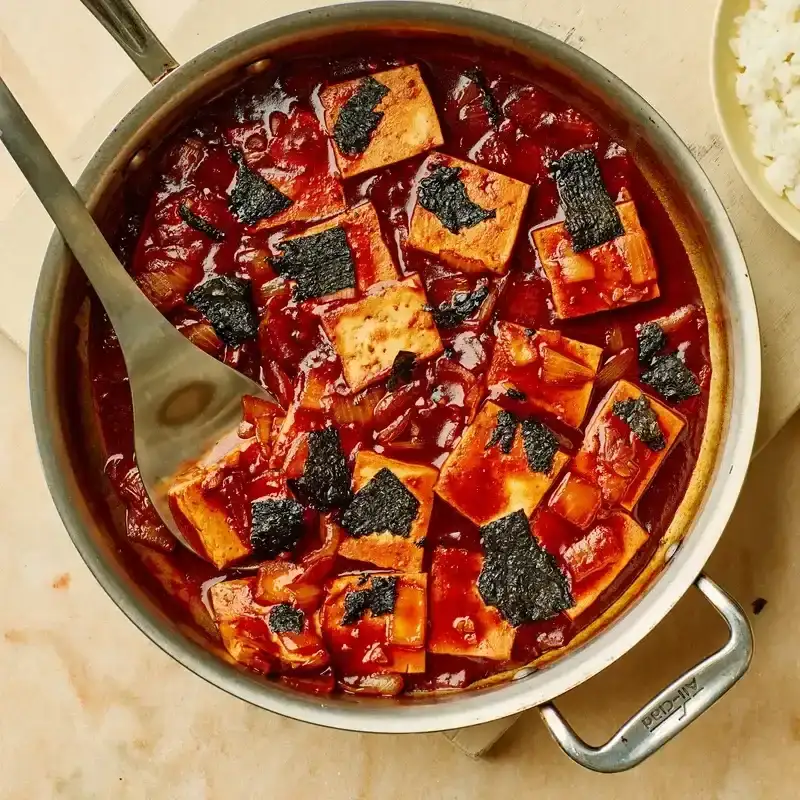 Gochujang-Butter-Braised Tofu in a stainless steel pan placed on top of a wooden surface