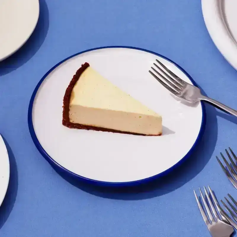 Slices of cheesecake with graham cracker crust on a blue background with forks to the side.