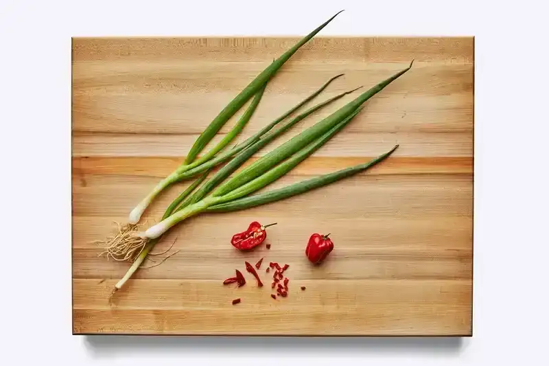 A Boos maple edge grain cutting board—one of the best cutting boards, according to BA editors—with scallions and peppers