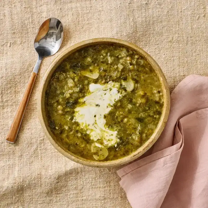 Lentil Soup With Greens and Rice in a brown bowl placed on a beige surface