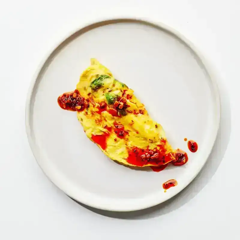 An egg omelet on a white plate with chili oil top of the omelet 