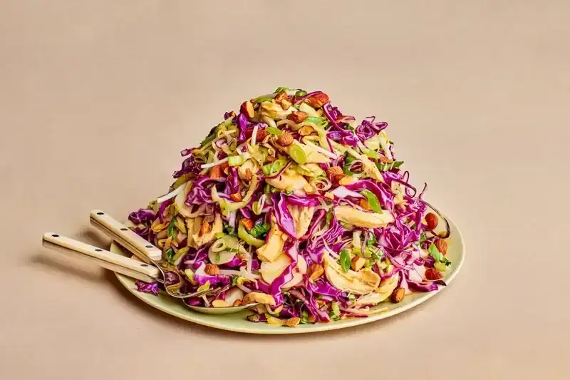 a mound of Purple cabbage salad with greens and chicken on a green plate 
