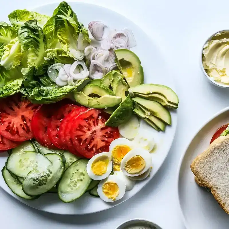 A platter with an easy lunch spread for making your own sandwiches with lettuce, sliced tomato, avocado, boiled eggs, shallots, and more.