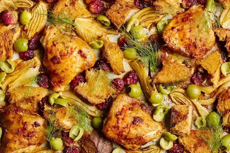 Roasted chicken thighs with fennel, grapes, olives, croutons, and dill on a sheet pan.