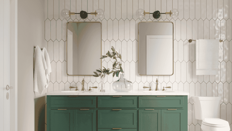 bathroom vanity with green cabinets, gold fixtures, and two mirrors and sconces, and a white tiled accent wall