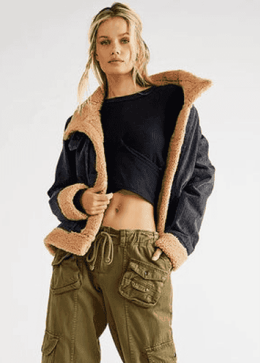 blonde model posing in olive green cargo pants, cropped black shirt, and a black fur-lined bomber jacket