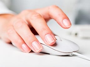 A hand clicks a mouse on a desk.