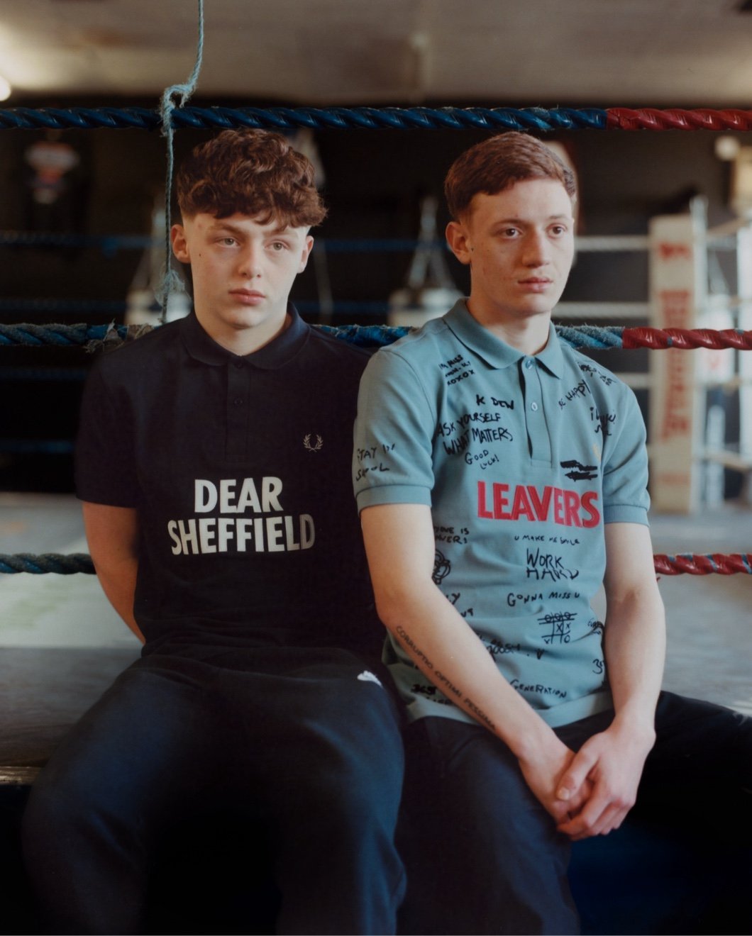 2 young men sat on the edge of a boxing ring, each wearing a different Corbin Shaw x Fred Perry collaboration Fred Perry Shirt