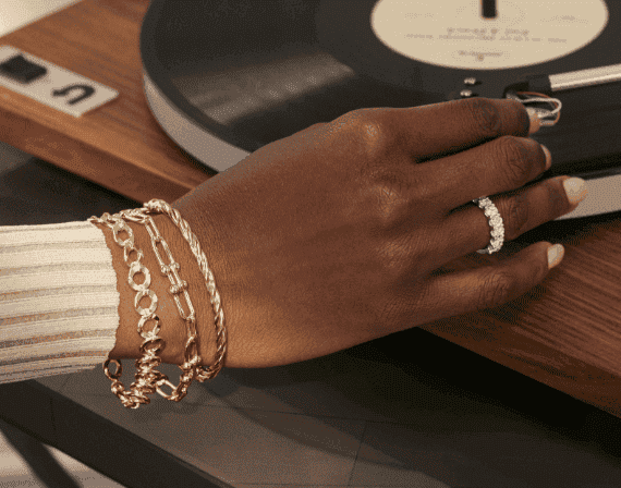 A hand can be seen dropping the needle on a record player. The hand show cases three gold bracelets and a diamond ring.