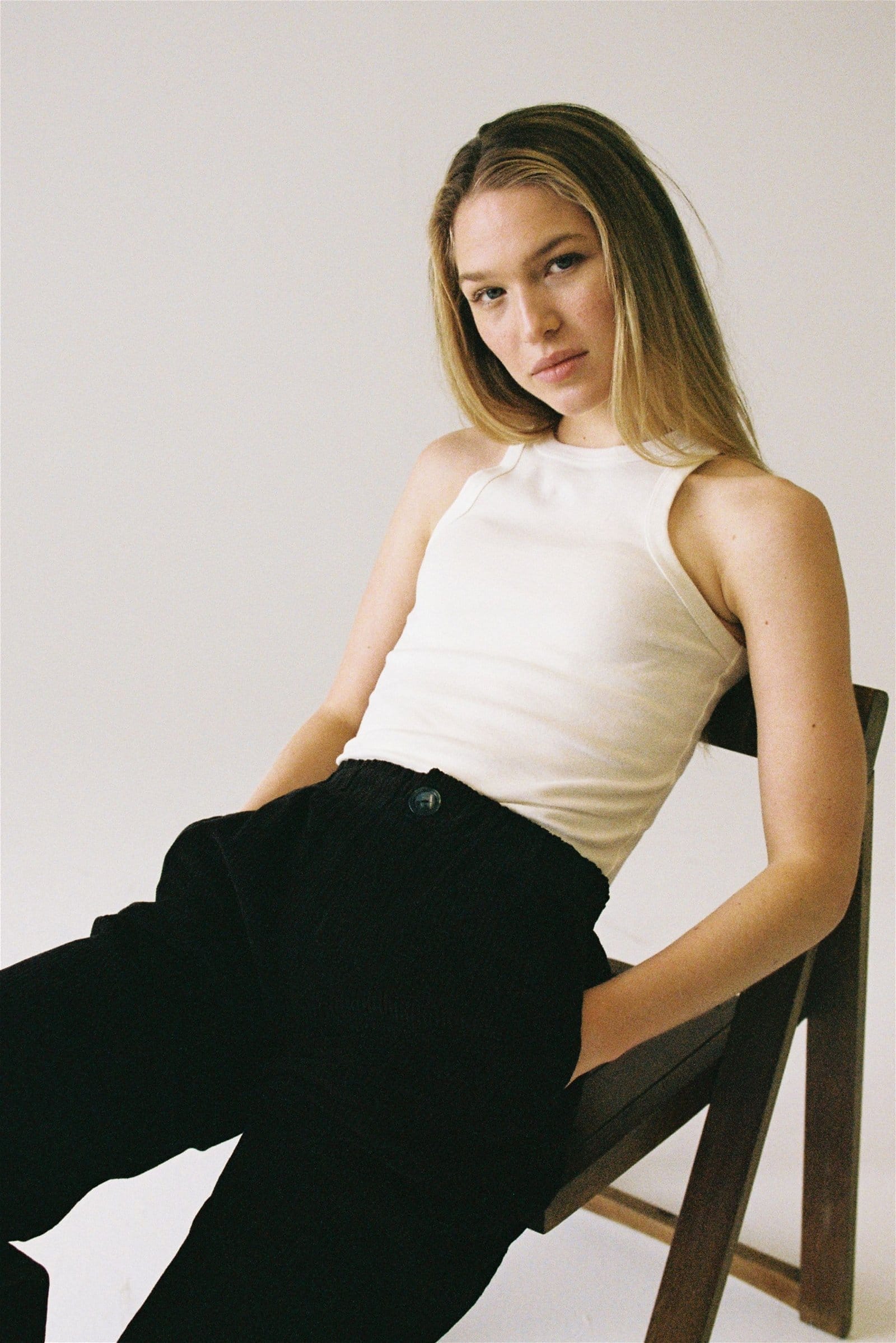 blond woman reclines on a folding chair wearing black pants and a white cotton halter tank looking at camera.