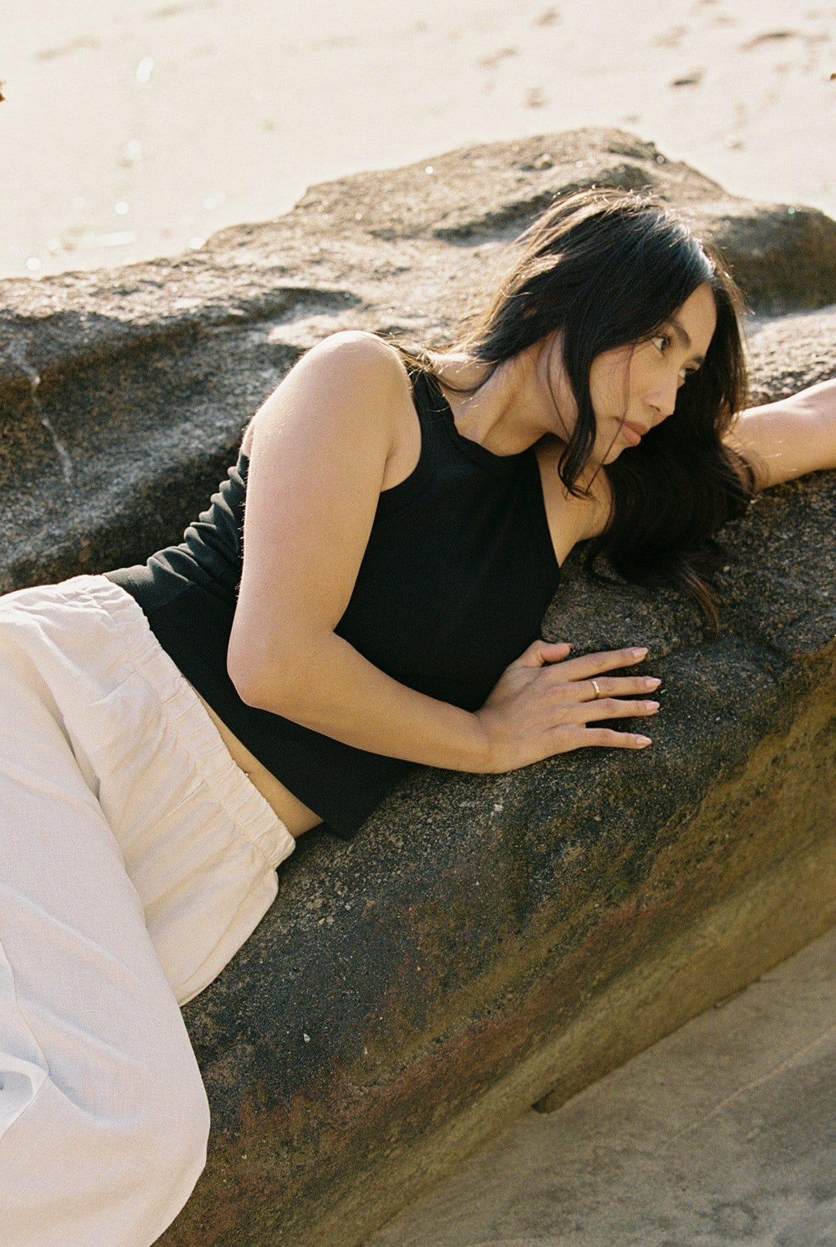woman lounges on a beach rock wearing a black cotton halter tank.