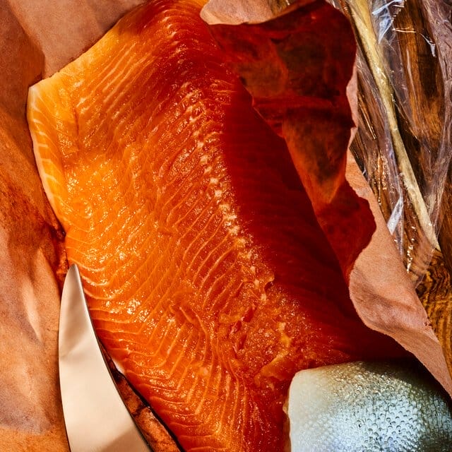 Closeup of a raw salmon filet on a shiny background; a knife sits alongside the filet.