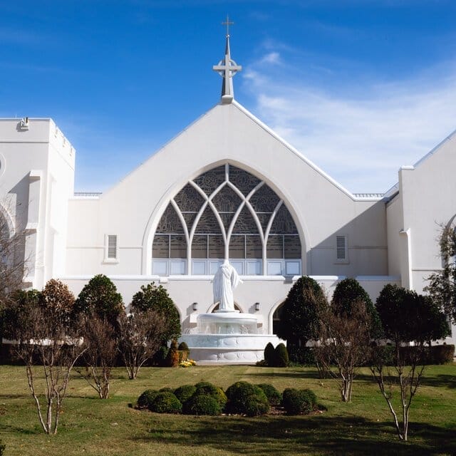 A white church on a clear day. In front of the church is a well-manicured lawn and small trees. 