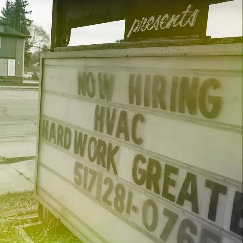 Person riding a bicycle past a sign that says %22NOW HIRING HVAC HARDWORK GREAT%22