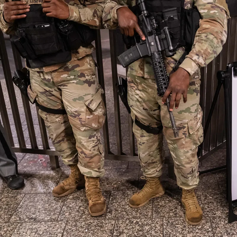 Two National Guard service members stand, holding weapons.