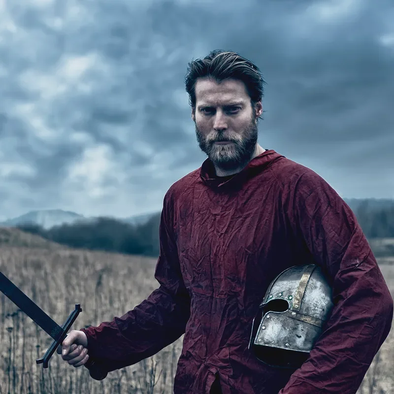 Person holding a sword and a knight helmet out in a field 