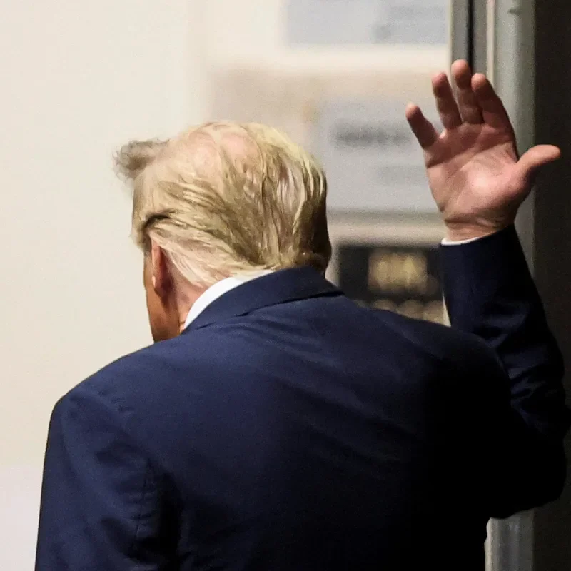 A photo of the former U.S. President Donald Trump walking in a Manhattan courthouse. Trump is gesturing with his right hand and is seen from behind.